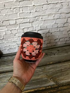 a hand holding a crocheted coffee cup cozy