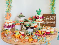 an assortment of cupcakes and desserts displayed on a table with cactus decorations