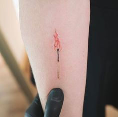 a person with a small tattoo on their arm holding a lit match in one hand