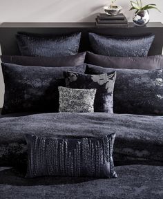 a bed with black and silver pillows on top of it next to a vase filled with flowers