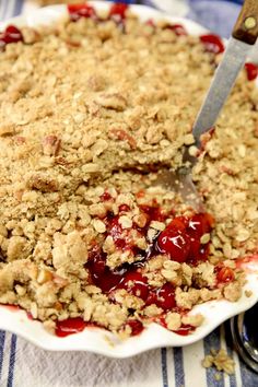 a pie with crumbled toppings on a white plate next to a fork