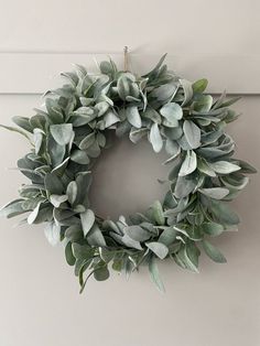 a wreath hanging on the side of a door with greenery in front of it