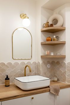 a white sink sitting on top of a wooden counter next to a shelf filled with bottles