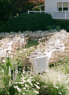 tables and chairs are set up in the garden for an outdoor wedding reception with white linens on them