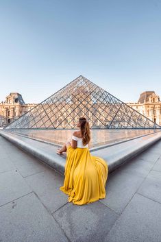 a woman sitting on the ground in front of a pyramid with a yellow skirt and white top