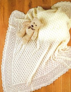 a teddy bear laying on top of a white crocheted blanket next to a wooden floor