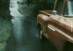 an orange truck driving down a wet road next to trees and bushes in the rain