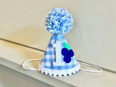 HAT: A party hat made of stiffened blue/white gingham fabric with white/blue #1, a cluster of blueberries next to it, trimmed with mini white pom poms on bottom and a blue/white yarn pom pom on the top.  Attached to a 1/8" elastic- to be worn comfortably like a headband.  *Can be made with any number- leave note in comments section  SIZE OPTIONS: MINI: $17.95 3" x 4.25" photos 1-2 SMALL:$19.95 4"x5.25" photo 3 shows size on 1 year old HIGH CHAIR BANNER: $26.95 3, 5" scallop shape blue gingham pennants, with white ONE and blueberry for the O. blue/white tassels on sides. Attached to a white 1/4" satin ribbon. *Add items individually to cart Playful Blue Hat For First Birthday, Berry Sweet 1st Birthday, Blueberry Party, Blueberry Birthday, First Birthday Hat, First Birthday Hats, Berry First Birthday, Yarn Pom Pom, White Tassel