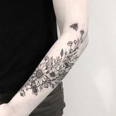 a woman's arm with flowers on it and a bee flying over the top