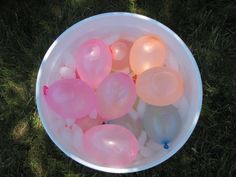 a bucket filled with lots of pink and white bubbley water balloons on top of green grass