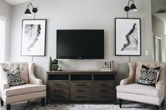 a living room with two chairs and a television mounted on the wall in front of it