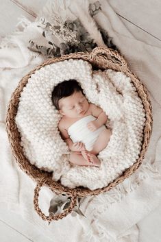 a newborn baby wrapped in a white blanket is laying on top of a wicker basket