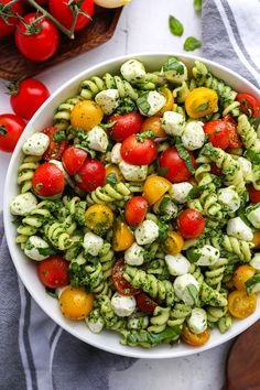 a white bowl filled with pasta salad next to tomatoes and broccoli on a wooden cutting board