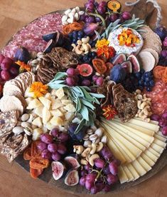 a platter filled with different types of cheeses and fruits on top of a wooden table