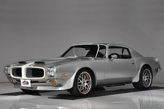 a silver muscle car sitting on top of a white floor next to a gray wall