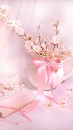 a vase filled with flowers next to an open book and pink ribbon on a table