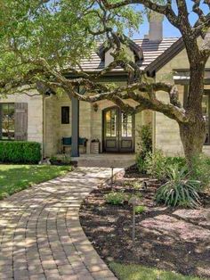 a house that has a tree in the front yard and brick walkway leading to it