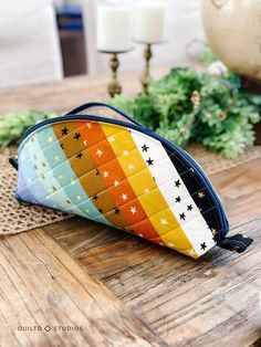 a colorful purse sitting on top of a wooden table next to candles and greenery