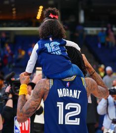 a man holding a child on his back in front of a crowd at a basketball game