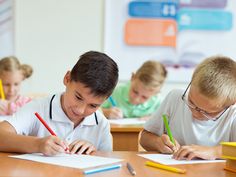 two young boys sitting at desk writing on paper with pencils in front of them