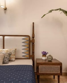 a bed sitting next to a night stand with a plant on top of it