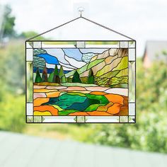 a stained glass window hanging from the side of a building with trees in the background