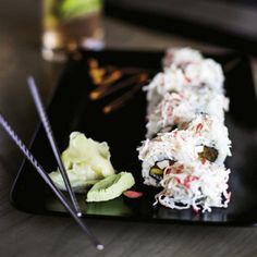 a black plate topped with sushi and chopsticks on top of a table