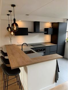 a kitchen with an island and bar stools next to the counter top, lights hanging from the ceiling