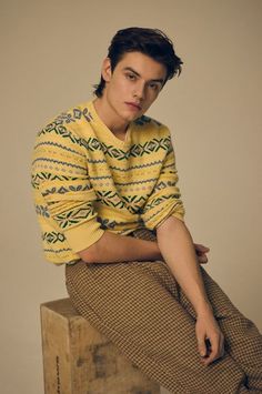 a man sitting on top of a wooden box wearing a yellow sweater and brown pants