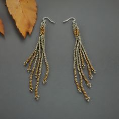 Drape yourself in elegance with these captivating Seed Bead Long Fringe Earrings that effortlessly blend gold and silver hues to form a stunning accessory piece. The intricate beadwork showcases a delicate fusion of colors, making them a versatile and chic addition to any outfit. As the elongated fringe gently sways with your every movement, these earrings exude a sense of grace and sophistication. Crafted with precision and attention to detail, these earrings boast a timeless design that complements various styles from casual to evening wear. The combination of seed beads in gold and silver tones creates a mesmerizing contrast that catches the light and adds a subtle sparkle to your look. Perfect for autumn and fall, these long fringe earrings are a celebration of artistry and craftsmansh Gift Idea For Girlfriend, Long Fringe, Long Fringes, Native Jewelry, Earrings Beaded, Earrings In Gold, Fall Accessories, Fall Jewelry, Dangling Earrings