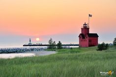 a red light house sitting on top of a lush green field next to the ocean