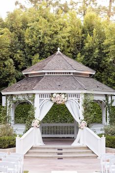 the gazebo is decorated with white flowers and greenery for an outdoor wedding ceremony