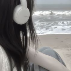 a woman sitting on the beach with headphones in her ears looking out at the ocean