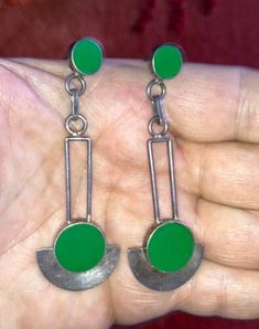 a pair of green and silver earrings in someone's hand