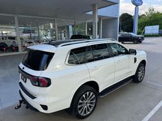 a white suv is parked in front of a car dealership with other cars behind it