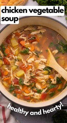 chicken vegetable soup in a large pot with a wooden spoon and bread on the side