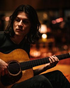 a man with long hair playing an acoustic guitar