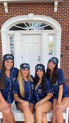 four young women in blue uniforms sitting on a bench outside the door of a building