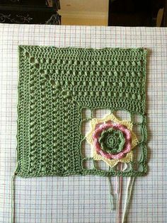 a green crocheted square with a flower on the front and side, sitting on a bed