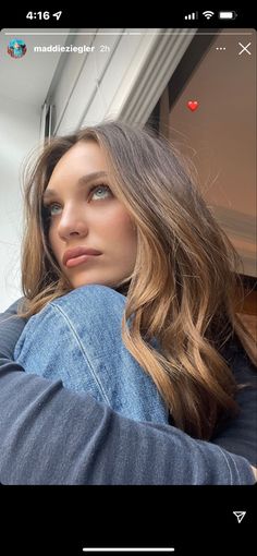 a woman with long hair leaning against a window sill and looking at the camera