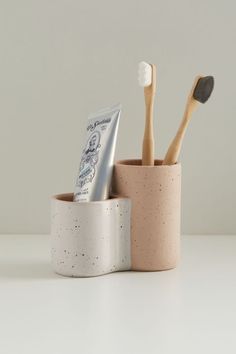 two toothbrushes in a cup next to each other on a white counter top