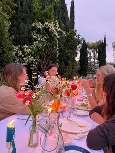 four women sitting at a table with plates and flowers in vases on the table