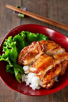 a red bowl filled with rice and meat next to chopsticks on a wooden table