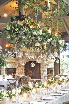 an image of a table set up for a wedding with candles and greenery hanging from the ceiling