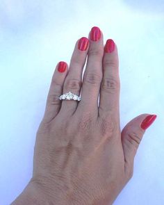 a woman's hand with red nail polish holding a diamond ring