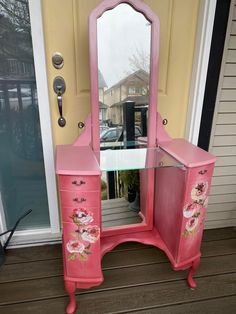 a pink vanity with flowers painted on the drawers and mirror in front of a door