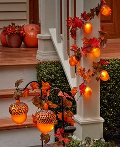 some pumpkins and leaves are hanging on the porch railing with lights attached to them