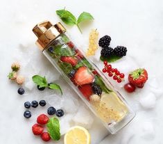 a bottle filled with lots of fruit on top of ice next to a lemon slice