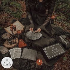 a woman is sitting on the ground surrounded by candles and other items that include books