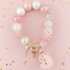 a pink bracelet with white beads and charms on it, sitting against a pink background